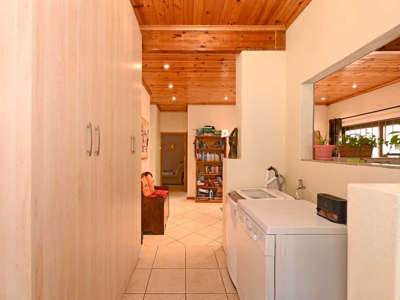 A functional laundry area featuring built-in cabinetry, tiled flooring, and a timber-clad ceiling, with a convenient pass-through window connecting to the adjacent living space.
