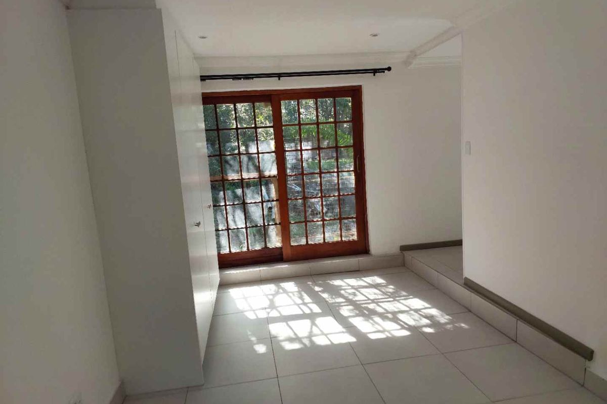 A bright, empty bedroom featuring tiled flooring, built-in cupboards, and wooden sliding doors providing access to the exterior.