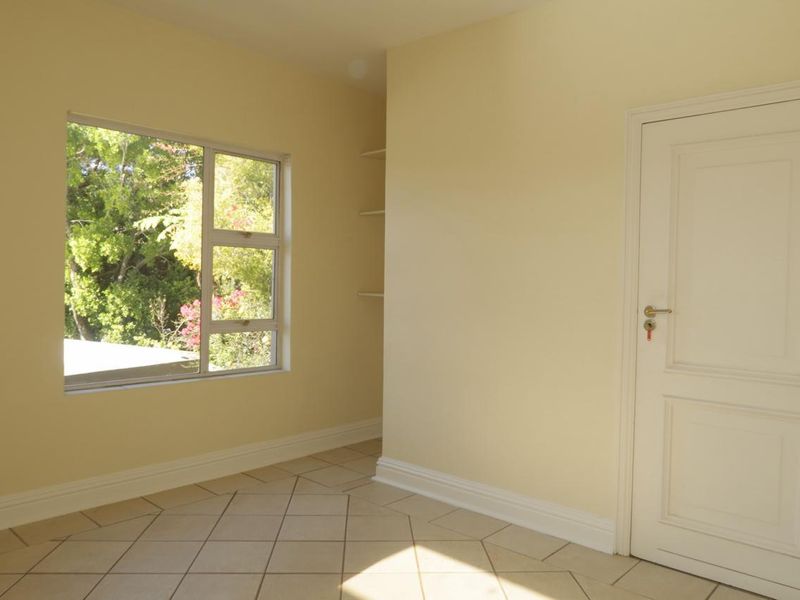 A bright, empty bedroom featuring tiled flooring, built-in shelving, and a window overlooking greenery.