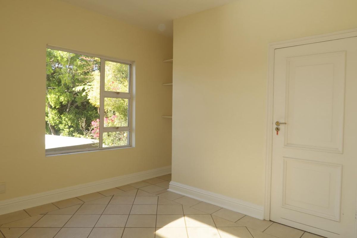 A bright, empty bedroom featuring tiled flooring, built-in shelving, and a window overlooking greenery.