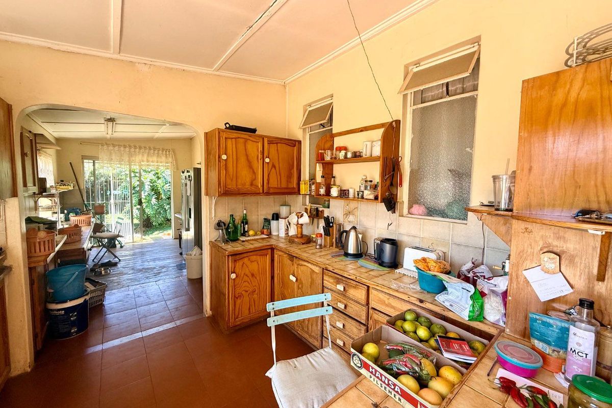 A dated kitchen featuring wooden cabinetry and tiled flooring, leading through an arched doorway to an adjacent living area with garden access.