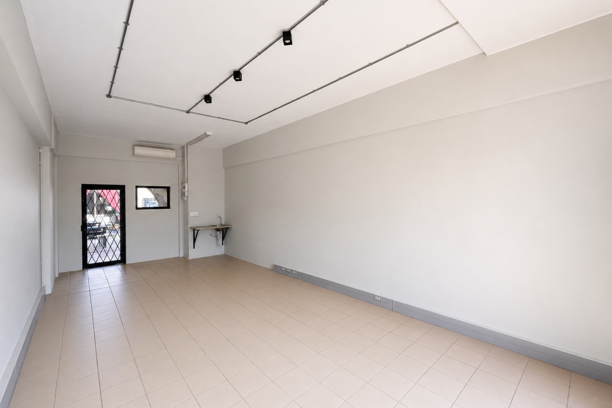 A clean, vacant open-plan retail space featuring tiled flooring, track lighting, a wall-mounted air conditioning unit, and a small utility sink.