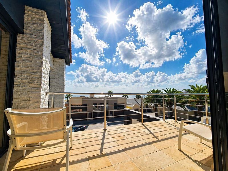 A sunny balcony featuring stone tile flooring and a modern stainless steel balustrade, offering an open view of the surrounding neighborhood.