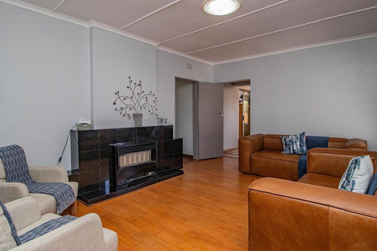 A comfortable living room featuring a dark tiled fireplace surround, laminate flooring, and classic ceiling paneling, providing a functional and inviting space.