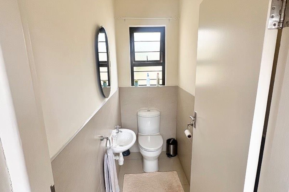A compact guest bathroom featuring a wall-mounted basin, a standard toilet, and neutral wall tiling.