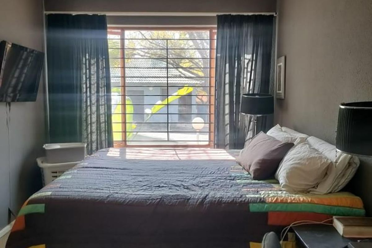 A bedroom featuring dark-toned walls and a large window fitted with security bars, providing natural light and a view of the exterior.