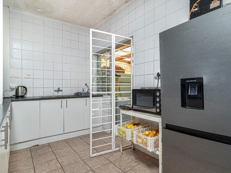 A functional scullery area featuring tiled walls, built-in cabinetry, and a stainless steel sink, requiring some maintenance and cosmetic updates.