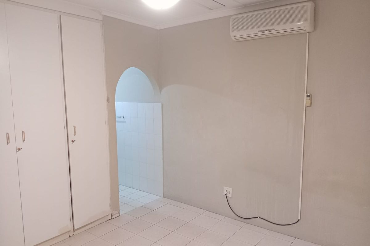 A clean, empty bedroom featuring tiled flooring, built-in cupboards, a ceiling fan, and a wall-mounted air conditioning unit.