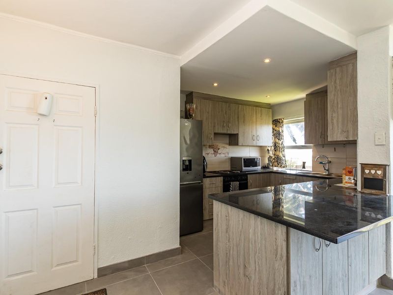 A functional kitchen featuring wood-look cabinetry, dark granite countertops, tiled flooring, and integrated appliances, offering a clean and practical cooking space.