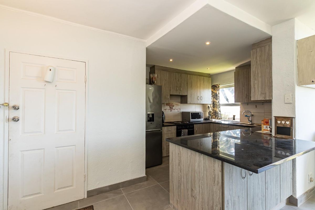 A functional kitchen featuring wood-look cabinetry, dark granite countertops, tiled flooring, and integrated appliances, offering a clean and practical cooking space.