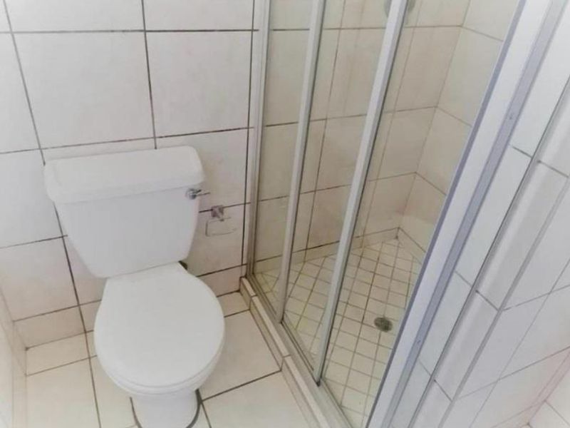 A functional bathroom featuring a standard toilet and a glass-enclosed shower with tiled finishes throughout.