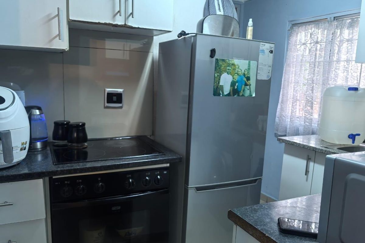 Compact kitchen featuring built-in cabinetry, electric hob, oven, and laminate countertops with security bars on the window.