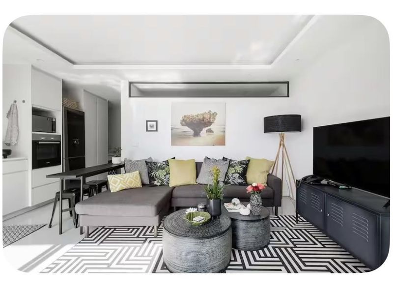 Modern open-plan living area featuring sleek white cabinetry, built-in kitchen appliances, recessed ceiling lighting, and polished floor tiles in a contemporary apartment setting.