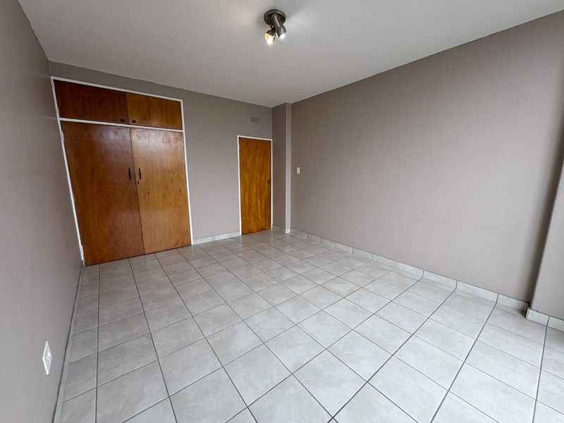 An empty bedroom featuring neutral wall paint, tiled flooring, and built-in wooden cupboards.