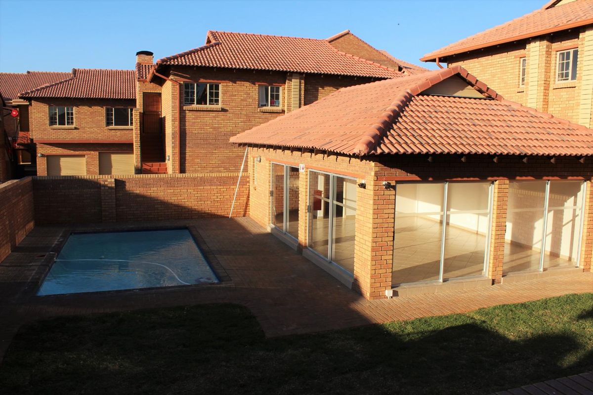 Rear view of a brick apartment complex featuring a private swimming pool, paved patio area, and sliding glass doors leading into the living space.