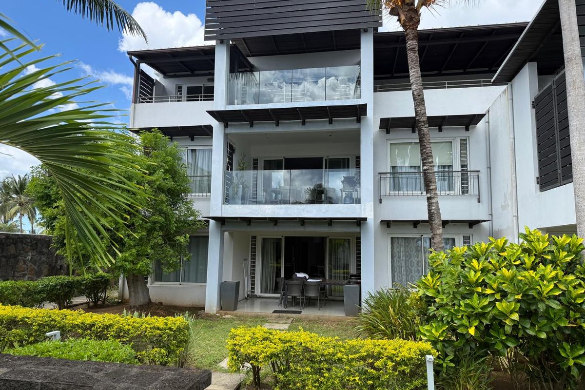 A view of the rear facade of a multi-story apartment building featuring private balconies with glass railings and a ground-floor patio area.