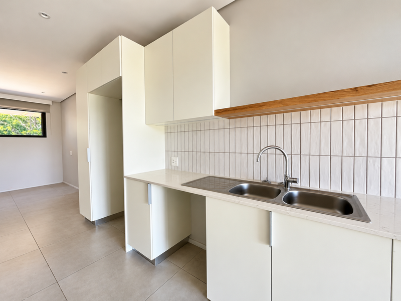 Modern kitchen featuring clean white cabinetry, stone countertops, a stainless steel double sink, and a stylish tiled splashback with a floating timber shelf.