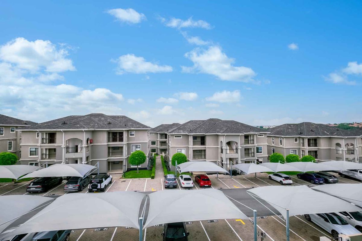 An elevated view of the apartment complex grounds, featuring paved parking areas with shade-cloth carports and well-maintained building facades.