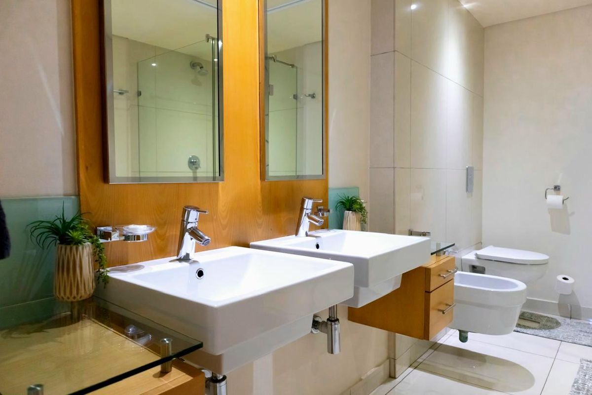 Modern bathroom featuring a double vanity with wall-mounted basins, wooden cabinetry, large mirrors, a glass shower enclosure, and a wall-hung toilet and bidet.
