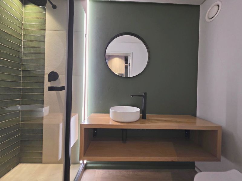 Modern bathroom featuring a floating wooden vanity, vessel sink with black fixtures, and a walk-in shower with stylish green tiled accents.