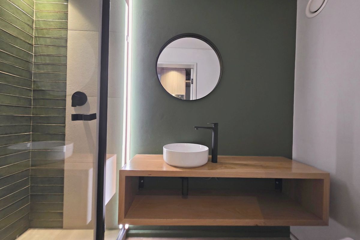 Modern bathroom featuring a floating wooden vanity, vessel sink with black fixtures, and a walk-in shower with stylish green tiled accents.