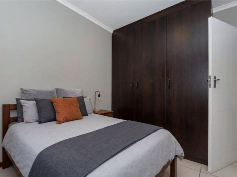 A well-maintained bedroom featuring dark wood built-in cupboards, neutral wall finishes, and tiled flooring.