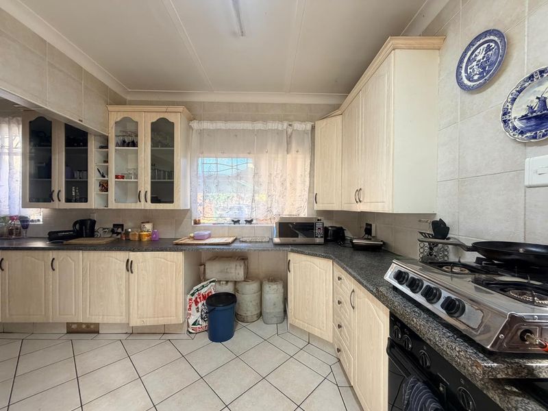 A functional kitchen featuring light-toned built-in cabinetry, dark laminate countertops, a gas stove, and tiled flooring with a classic backsplash.