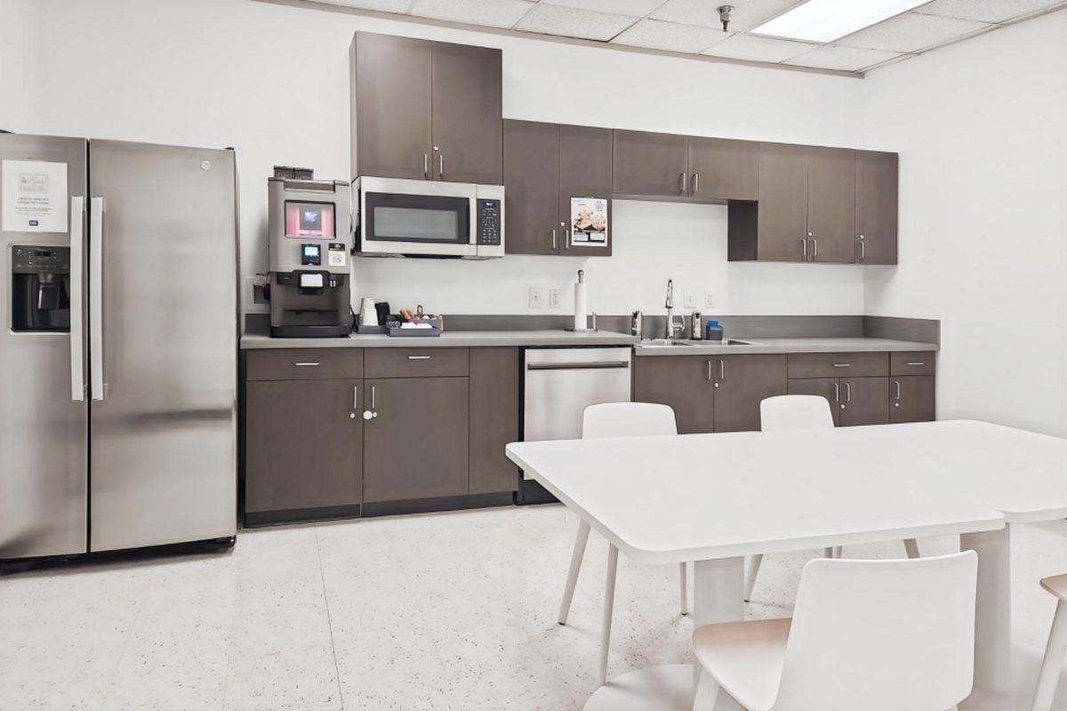 A functional office kitchenette featuring modern dark cabinetry, stainless steel appliances, a built-in microwave, and a drop ceiling with integrated lighting.