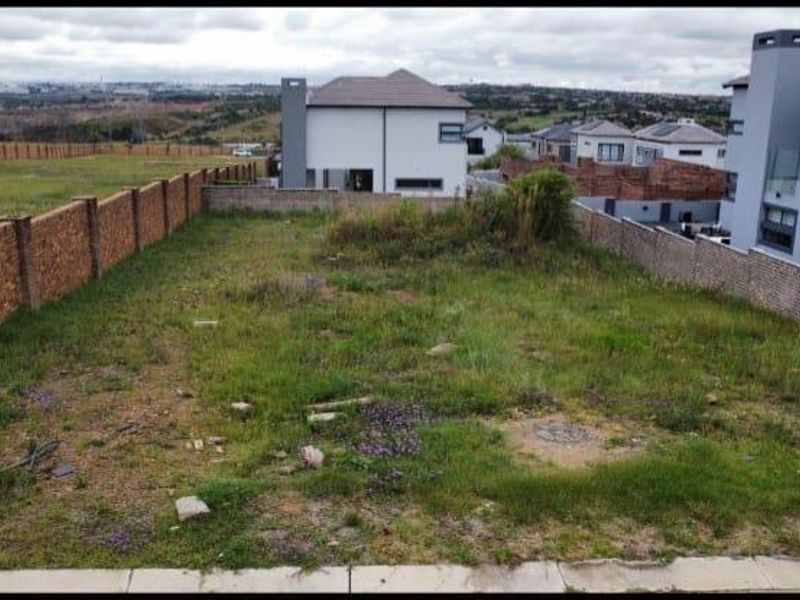 A vacant residential plot featuring a brick boundary wall and natural grass coverage, situated in a developed estate.