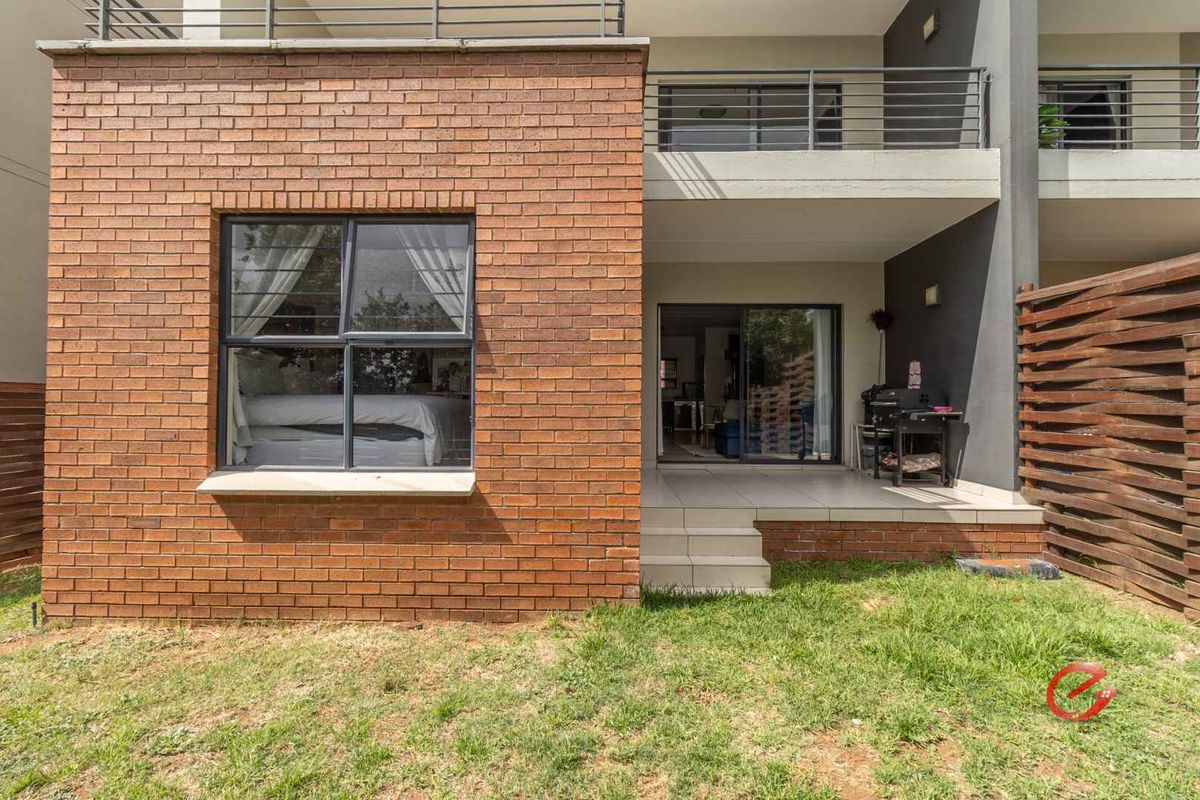 Rear view of the apartment featuring a brick facade, a covered patio area, and a small private garden space.