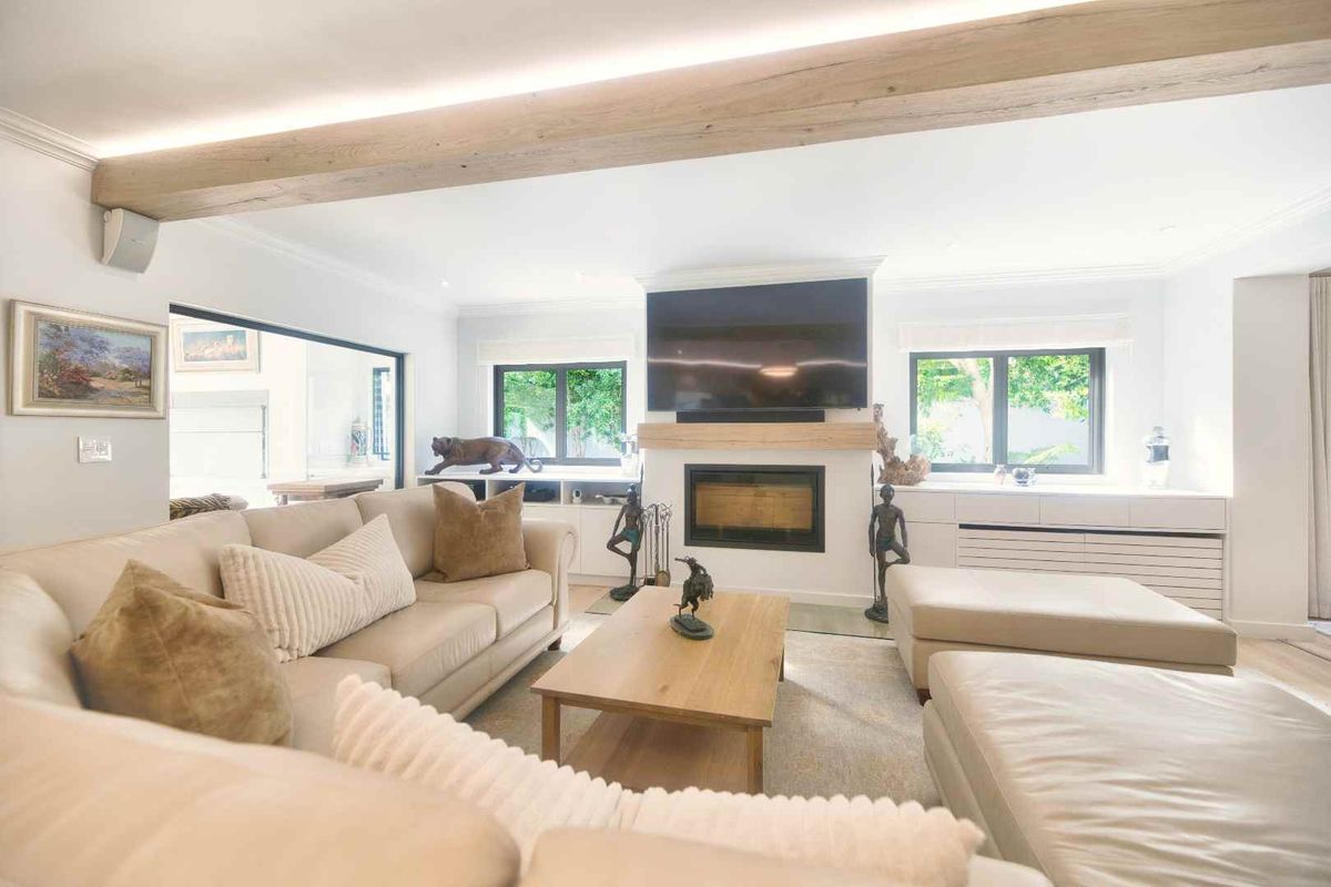 A bright and modern living room featuring a built-in fireplace, exposed timber ceiling beam, and custom built-in cabinetry with recessed lighting.