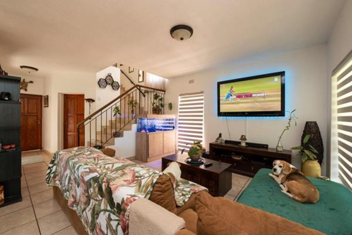 A spacious living room featuring tiled flooring, a staircase with metal railings, and wall-mounted television setup.