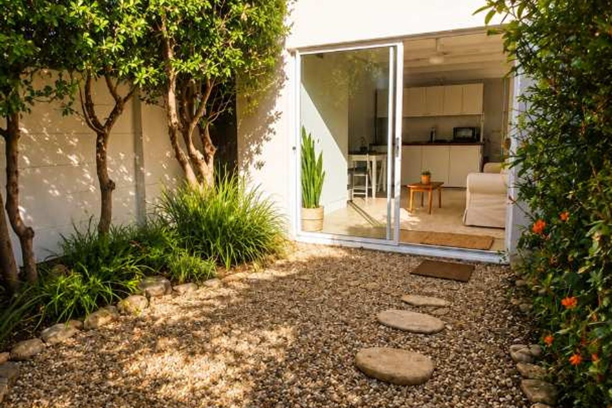 A private rear courtyard featuring a gravel garden with stone stepping stones and a sliding glass door providing access to the interior living space.