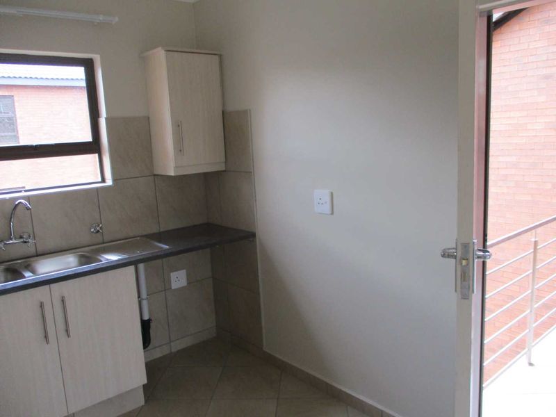 A clean, functional scullery area featuring built-in cabinetry, a stainless steel sink, tiled splashbacks, and direct access to an outdoor balcony.
