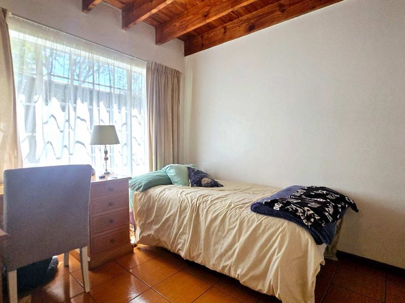 A cozy bedroom featuring exposed timber ceiling beams, tiled flooring, and a large window that allows for natural light.