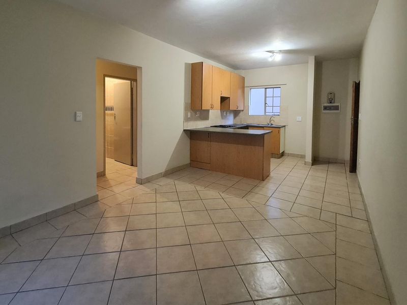 An open-plan living and kitchen area featuring tiled flooring, built-in wooden cabinetry, and a functional kitchen peninsula.