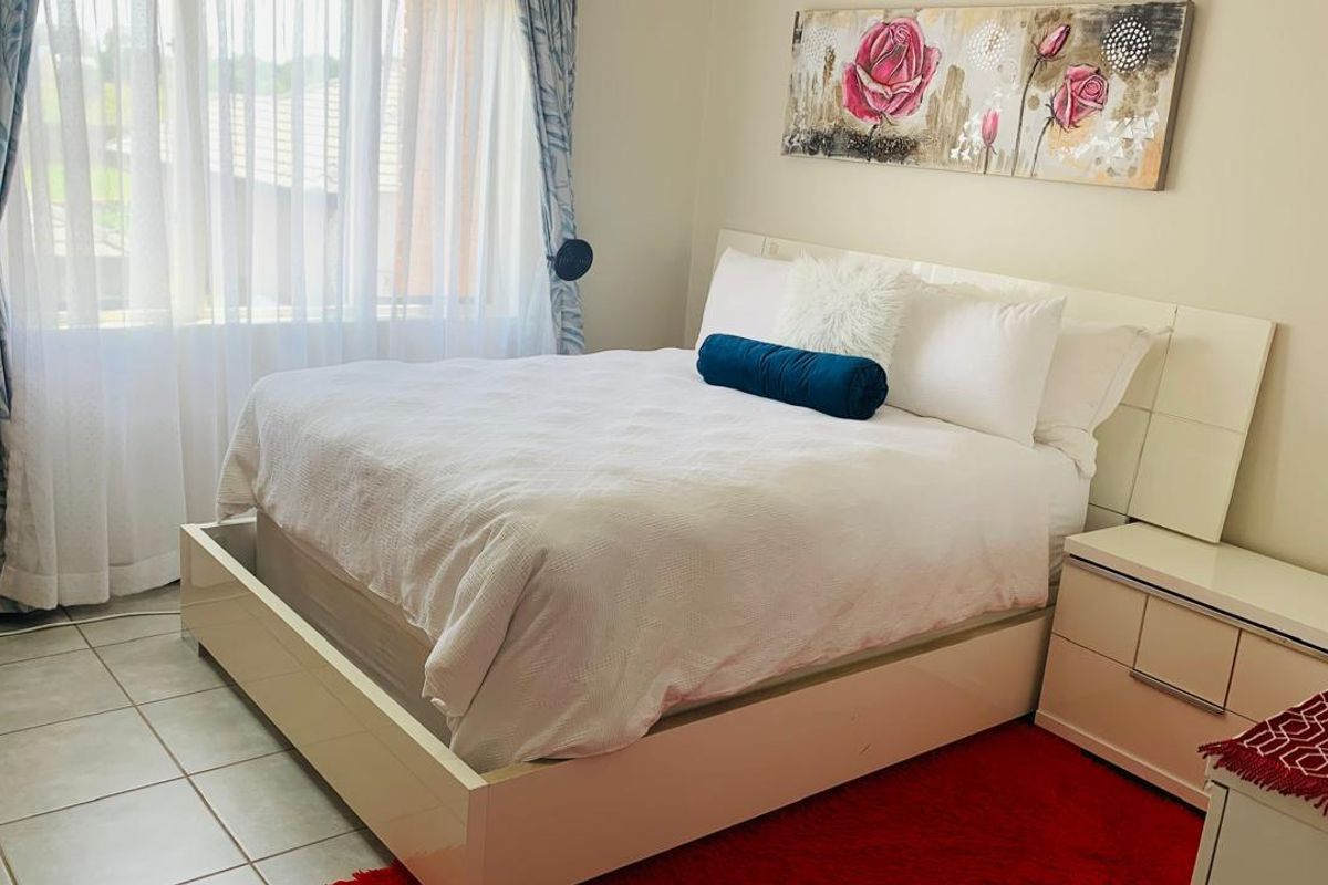 A well-lit bedroom featuring tiled flooring and large windows with sheer curtains, providing a bright and comfortable living space.