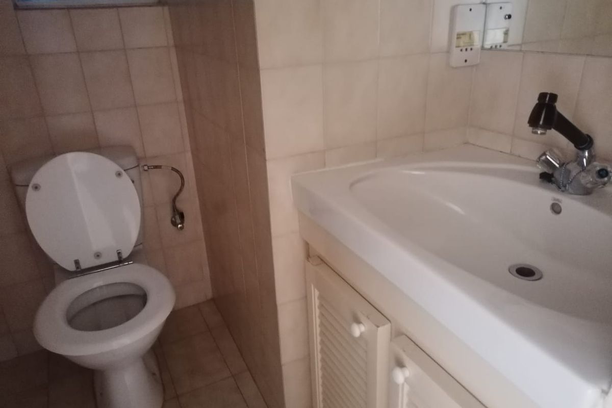 A compact bathroom featuring a standard toilet, a vanity basin with storage cabinetry, and tiled wall finishes.