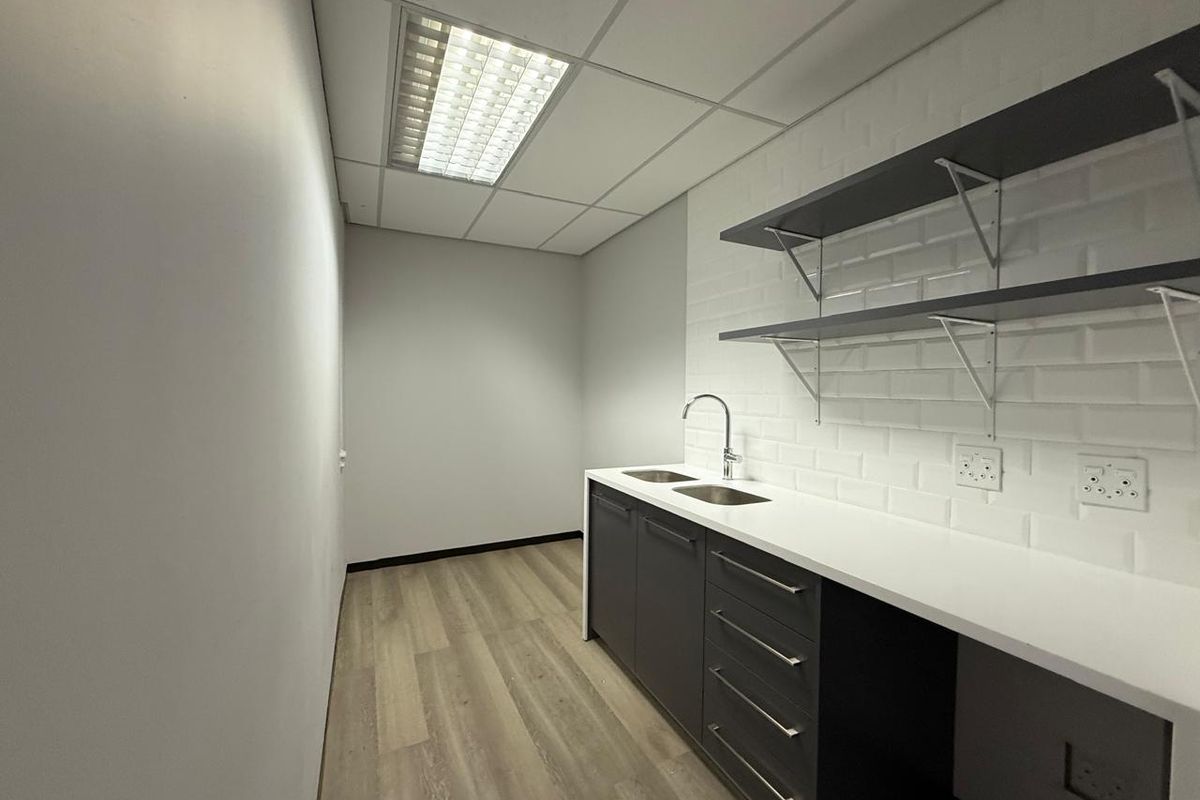 A clean, modern kitchenette featuring dark cabinetry, white subway tile backsplash, open shelving, and a stainless steel sink in a professional office setting.