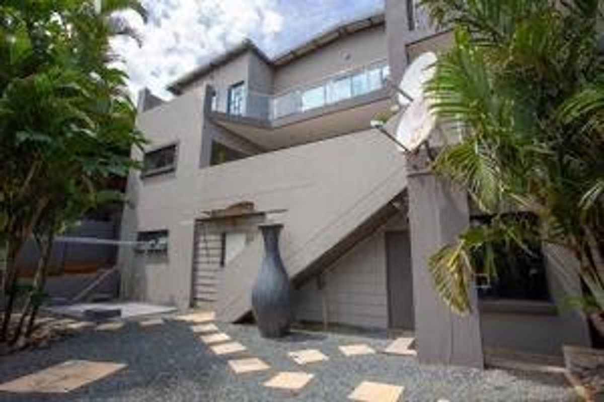 Rear view of a multi-story residential property featuring a paved patio area, external staircase, and balcony with glass balustrades.