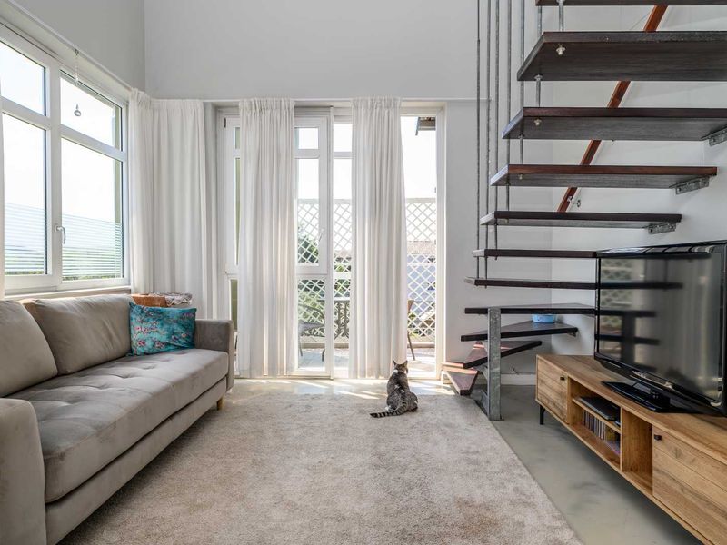 Bright living room featuring a modern floating staircase, concrete flooring, and large glass doors leading to an outdoor area.