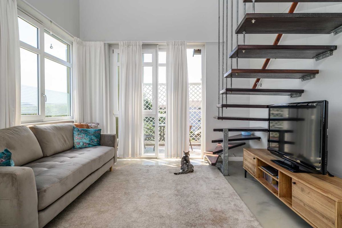Bright living room featuring a modern floating staircase, concrete flooring, and large glass doors leading to an outdoor area.