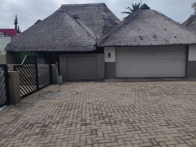 Front elevation of a cluster home featuring a traditional thatched roof, double garage, and paved driveway with secure gated access.
