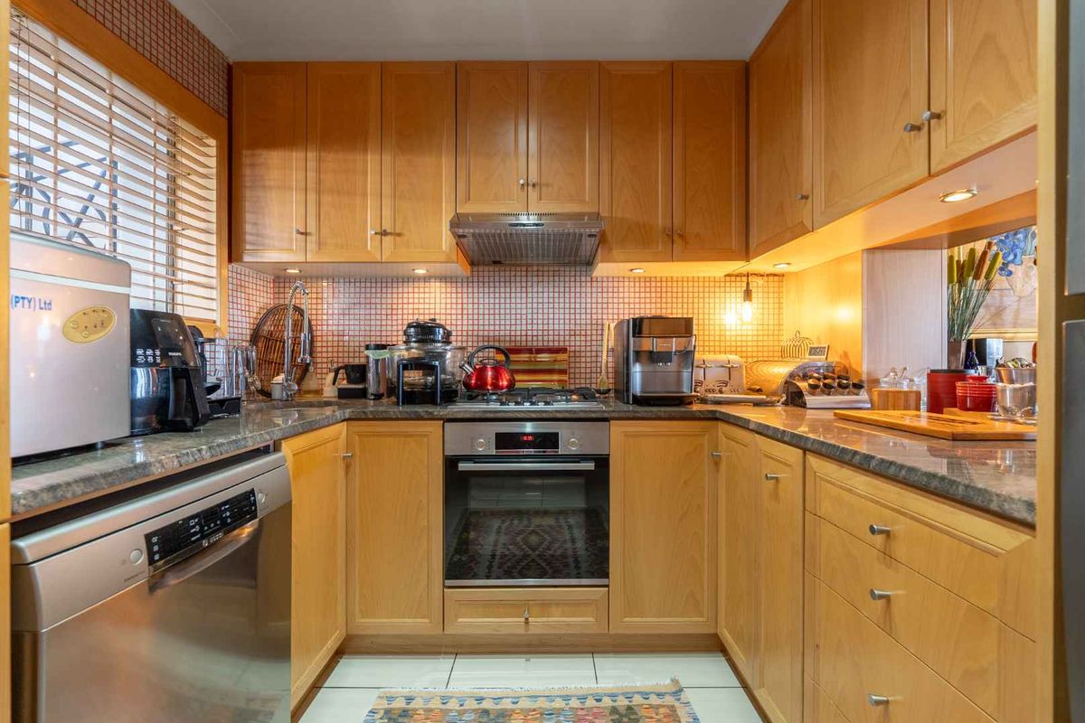 A functional U-shaped kitchen featuring warm wooden cabinetry, granite countertops, a mosaic tile backsplash, and integrated stainless steel appliances.