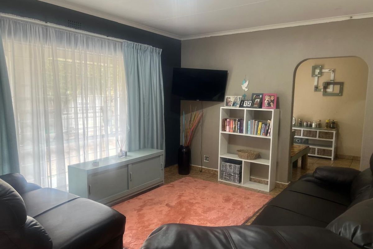 A comfortable living room featuring tiled flooring and an arched entryway leading to an adjacent space, with natural light provided by a large window.