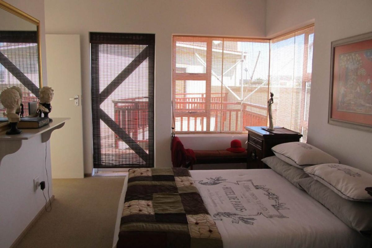 A bright bedroom featuring large corner windows with integrated blinds and direct access to an outdoor balcony area.