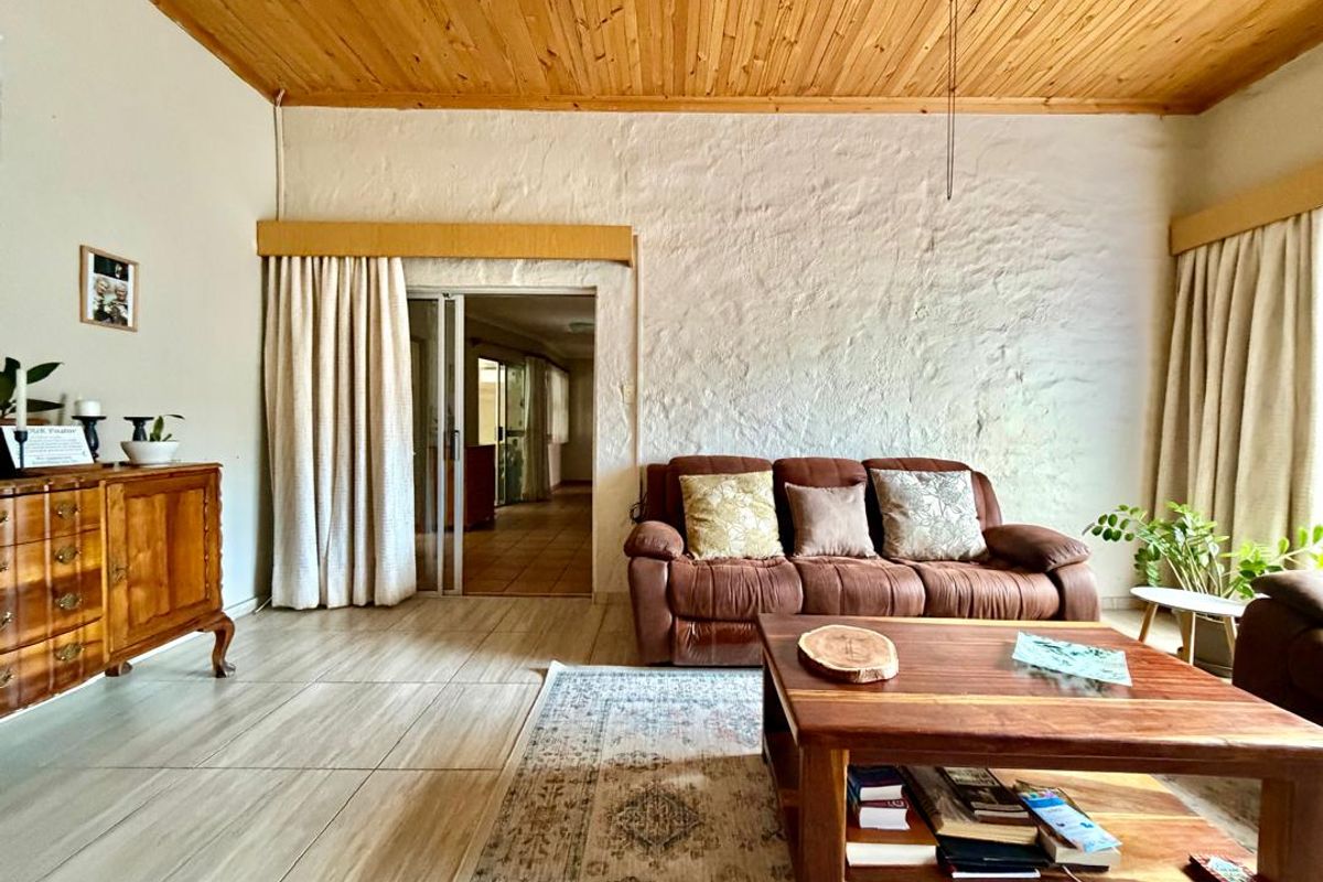 A living room featuring a textured white wall, wood-paneled ceiling, and tiled flooring, with a sliding door leading to an adjacent space.