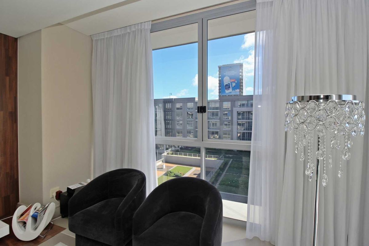 A bright living area featuring large floor-to-ceiling windows with views of the surrounding urban landscape and complex grounds.