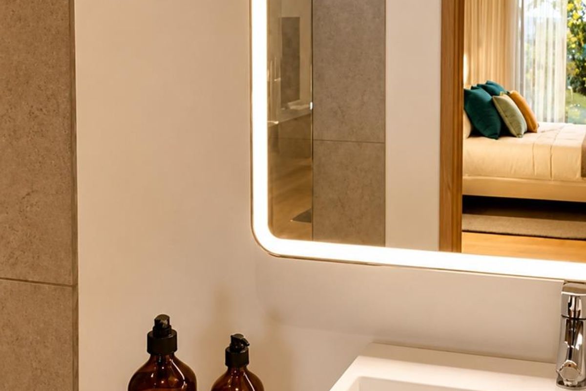 A modern bathroom vanity featuring a sleek basin, chrome faucet, and a contemporary backlit mirror, with a view into the adjacent bedroom.