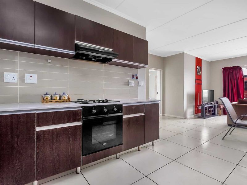 Open-plan kitchen and living area featuring dark wood cabinetry, built-in oven, gas hob, and neutral tiled flooring throughout the space.